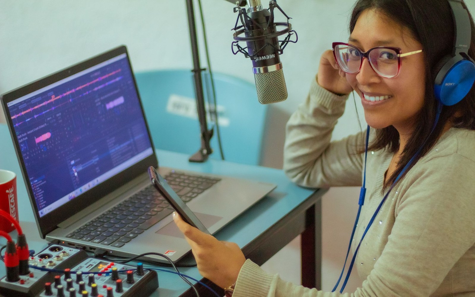 Podcast recording desk with a large-diaphragm microphone, audio interface, and foam panels, adult seated at the position